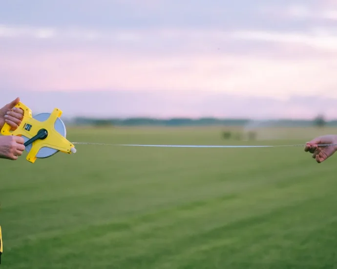 Two people stretching a tape measure across a field